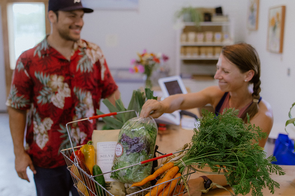 New Roots Community Farm customer checking out with a cashier, with a basket full of fresh vegetables.