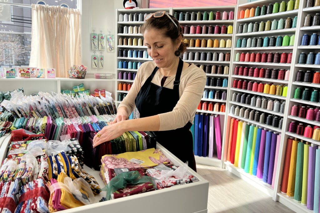 Female BIPOC business owner sorting through fabrics in her store.